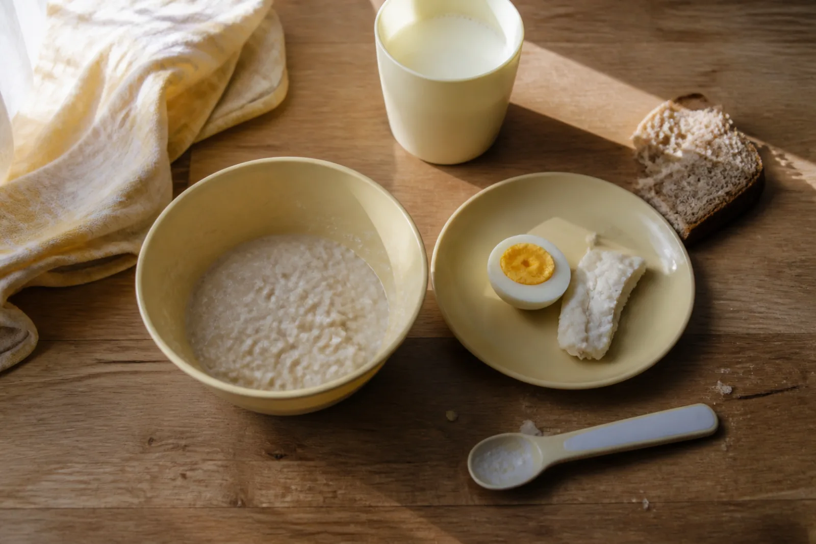 Тарелка с половинкой яичного желтка, кусочком рыбы, овсяной кашей и кружкой кефира на кухонном столе